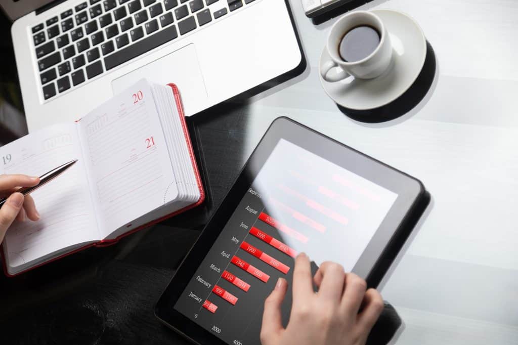 Close-up of hands making notes in diary next to tablet computer